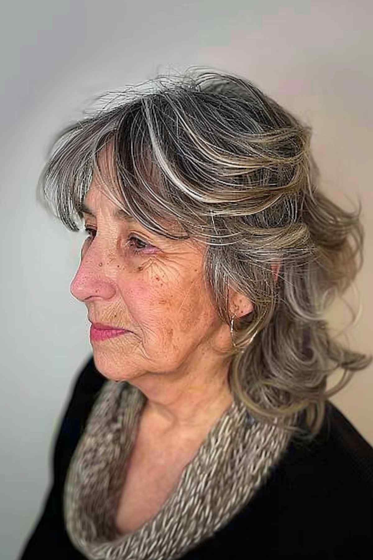 A middle-aged woman with an uncoiffed shag cut and casual bangs that show off her natural wavy hair, offering an easy-to-maintain textured style.